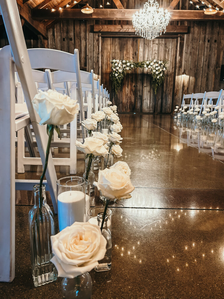White roses in bud vases down a wedding ceremony aisle.