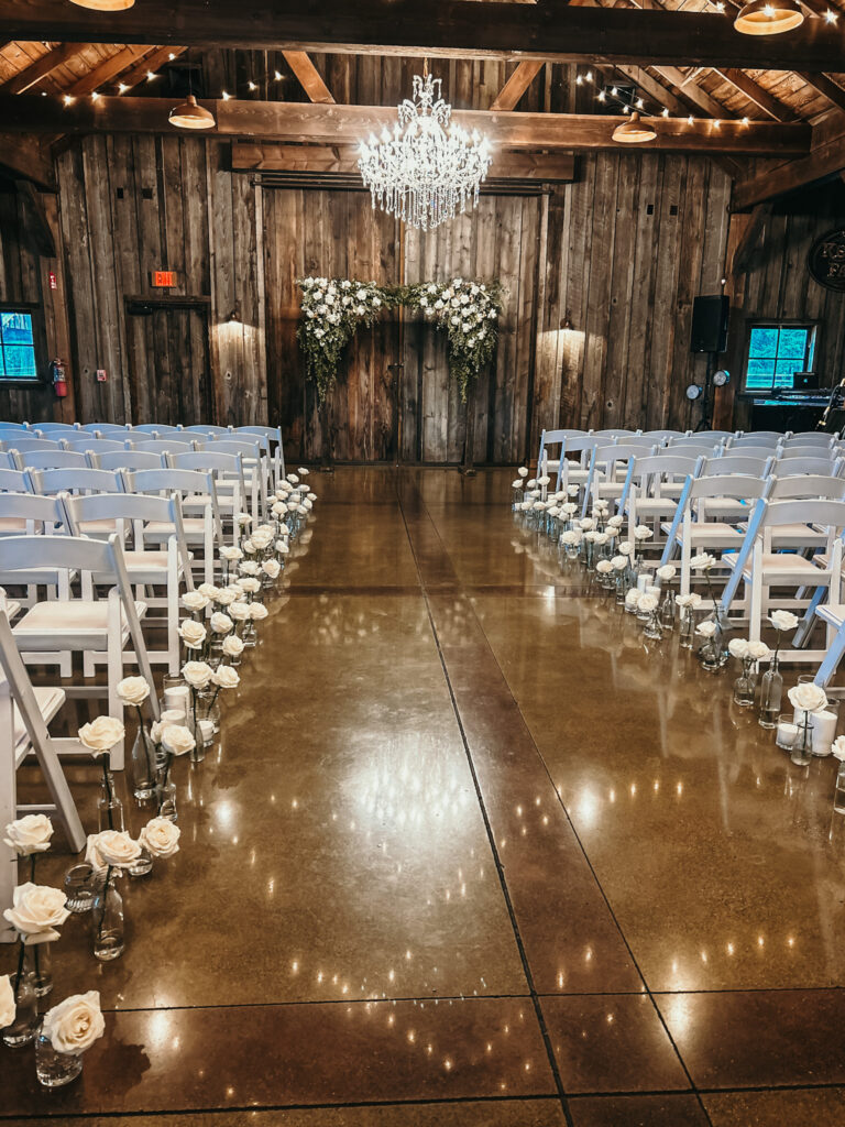 White roses in bud vases down a wedding aisle.