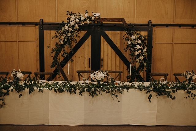 Vining greenery and white flowers on arch and head table at wedding reception. Ever Blooming Floral, Puyallup, WA.